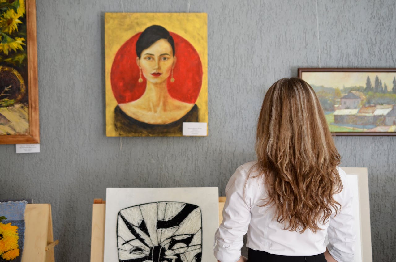 A woman views paintings in an art gallery, appreciating various art styles on display.